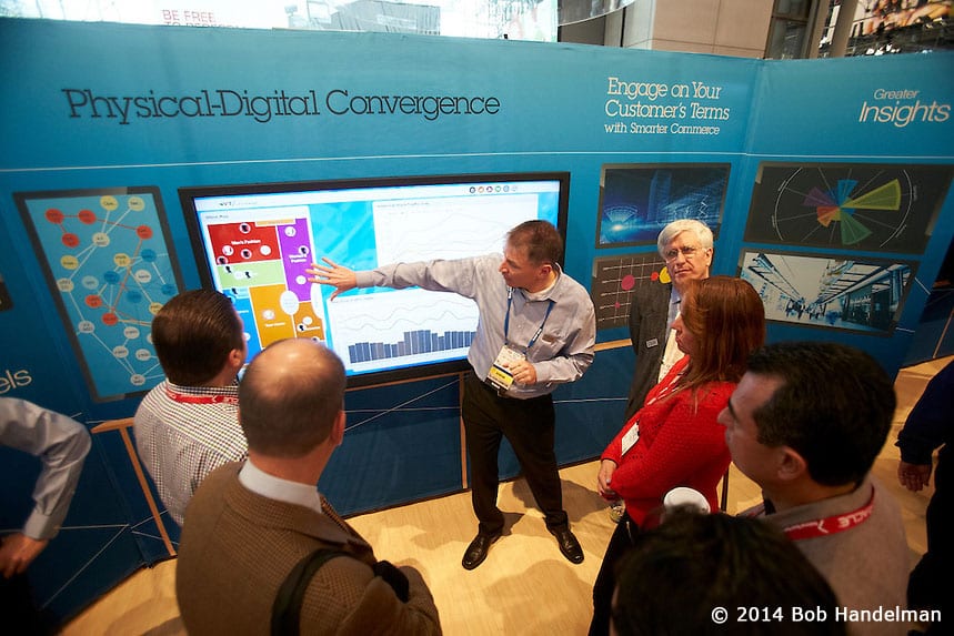An IBM presenter demonstrating on a large screen in the Physical-Digital Convergence area to a crowd