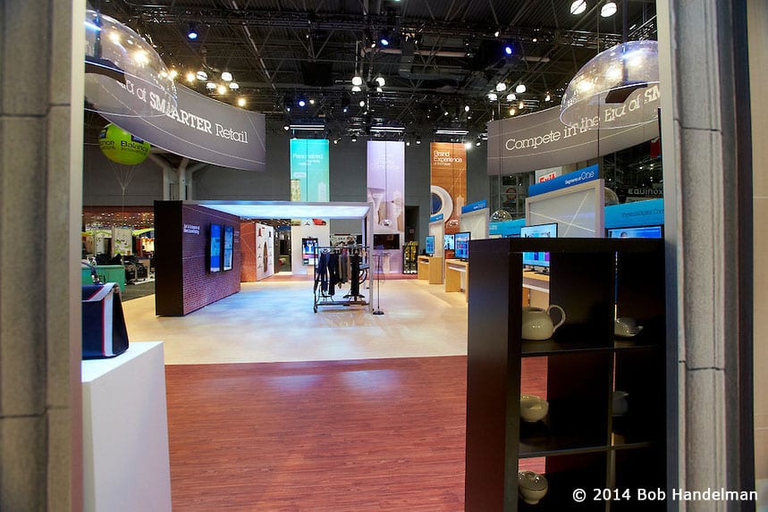 View through the IBM booth toward the clothing racks and demo areas, under the Smarter Retail signs