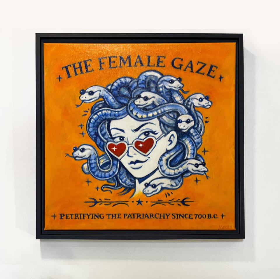 Square framed artwork featuring a Medusa-like figure with snakes for hair, wearing heart-shaped sunglasses. The artwork is set against an orange background with the text "THE FEMALE GAZE" and "+ PETRIFYING THE PATRIARCHY SINCE 700 B.C. +".