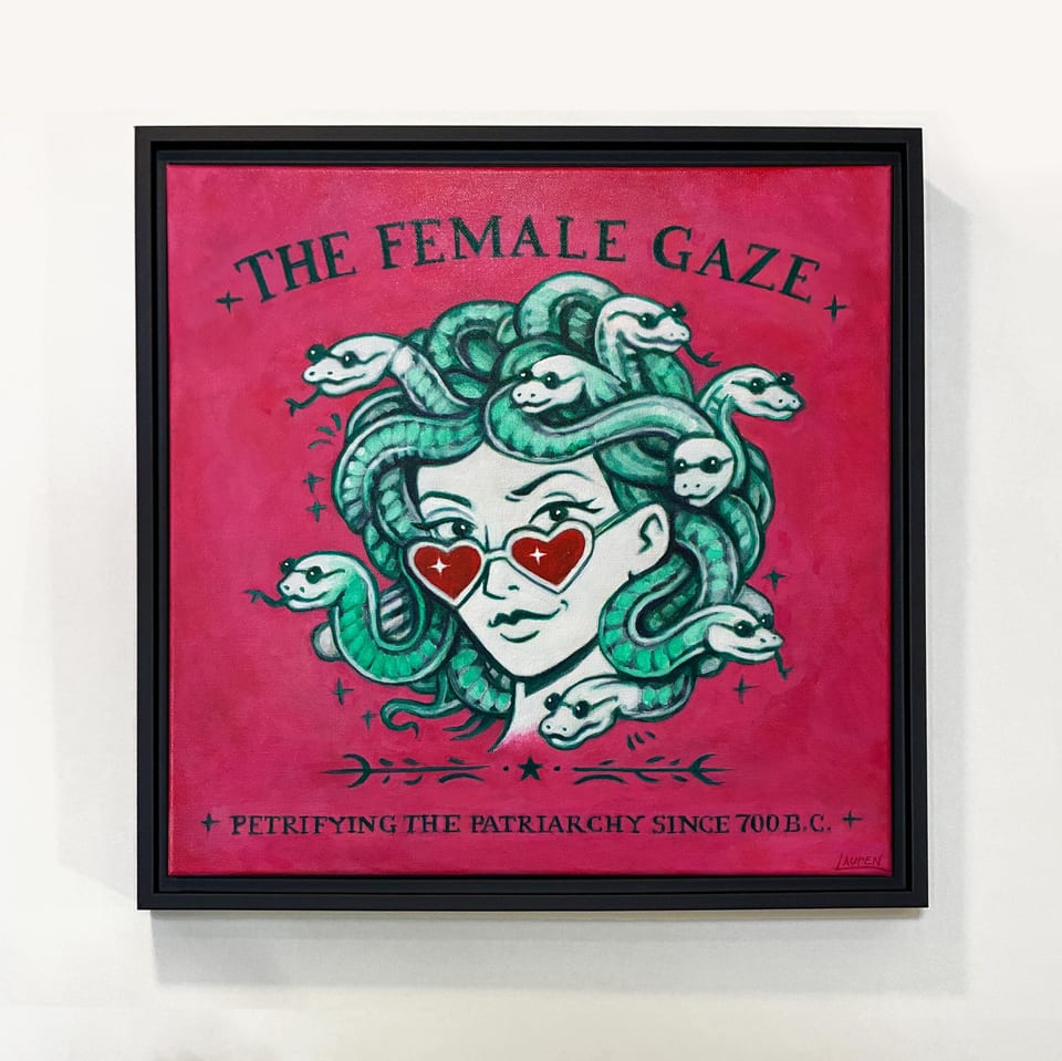 Square framed artwork featuring a stylized illustration of Medusa with snakes for hair. She wears heart-shaped sunglasses. The text "THE FEMALE GAZE" and "PETRIFYING THE PATRIARCHY SINCE 700 B.C." are displayed on a pink background.