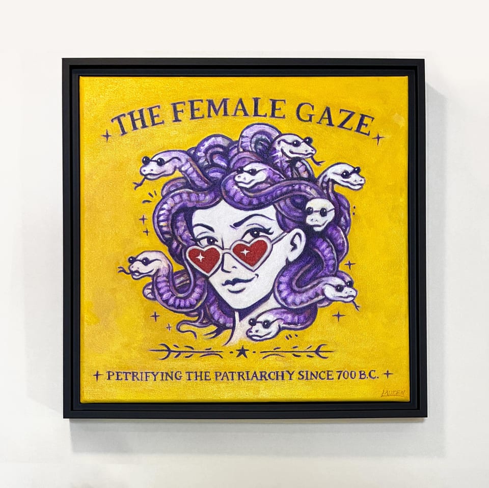 Square framed artwork featuring a Medusa illustration with purple snakes for hair, wearing heart-shaped sunglasses. The background is yellow with the text "THE FEMALE GAZE" and "+ PETRIFYING THE PATRIARCHY SINCE 700 B.C. +"